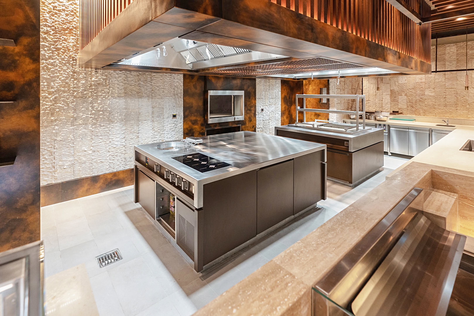 Professional kitchen with a stainless steel cooking island beneath a full-width extraction canopy