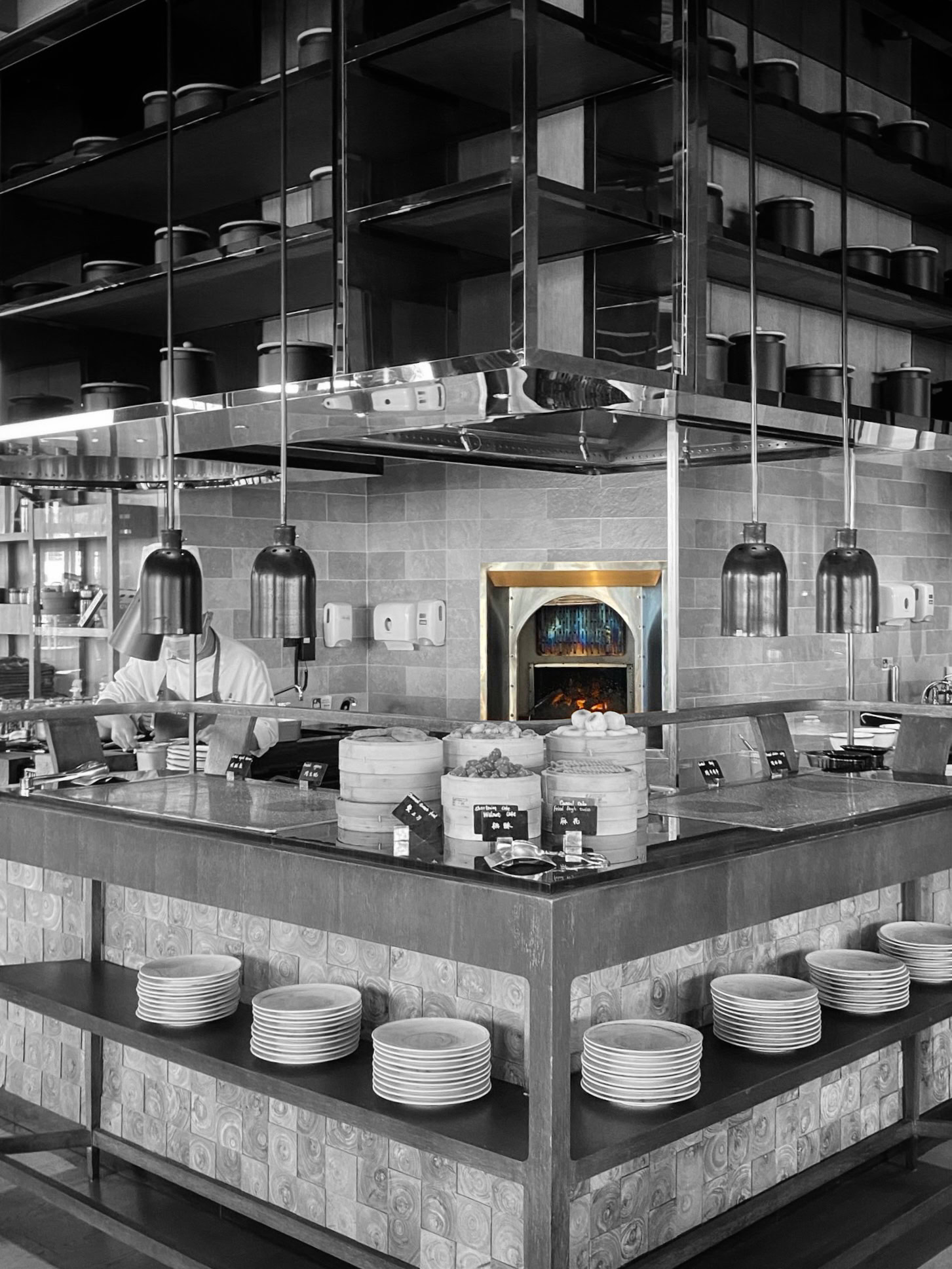 Lit oven at the centre of a stainless steel display kitchen hung with pendant lamps