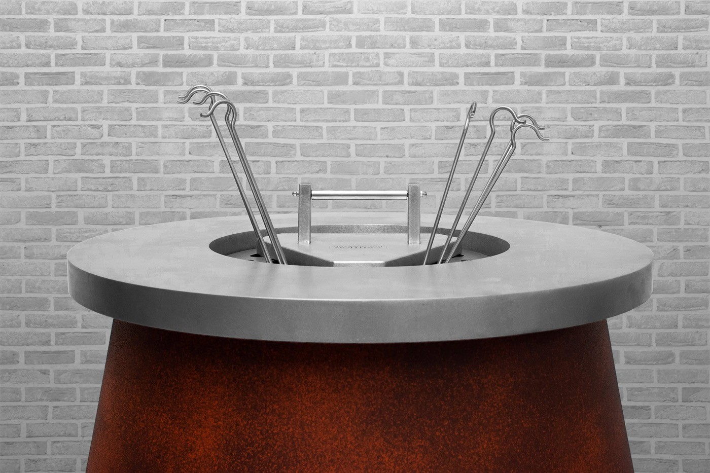 Cylindrical tandoor with a copper body and concrete rim, skewers resting in the opening